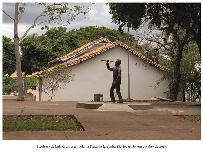 4 z 2- Escultura de Luiz Cruls assentada na Praça da Igrejinha São Sebastião, em outubro de 2018. Tablado construído de cimento acinzentado, onde está afixada a escultura de Luiz, de perfil segurando uma luneta na mão direita. Realização: Academia Planaltinense de Letras, Artes e Ciências (APLAC), pelo Ecomuseu Pedra Fundamental e pelo Coletivo Nativo Audiodescrição produzida  pelo Instituto de Promoção das Pessoas com Deficiência Visual Audiodescritora: Elma Lúcia Rodrigues Consultor: Fernando Rodrigues Este projeto é promovido com recursos do Fundo de Apoio a Cultura do DF